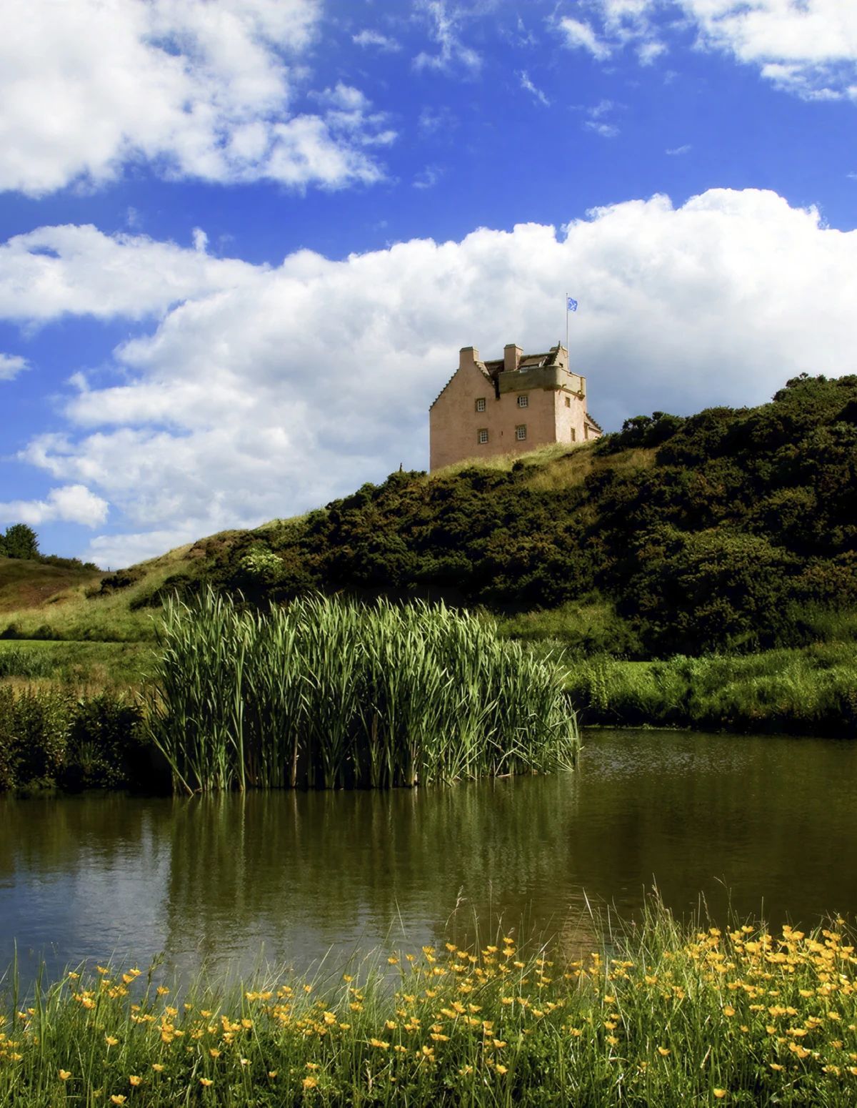 Un château perché sur une colline, avec une étendue d’eau au premier plan.