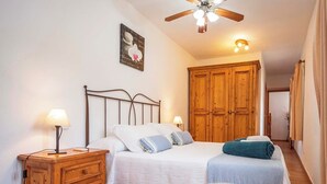 A bedroom with a bed, bedside tables, a wooden wardrobe, a ceiling fan, and a wall-mounted light fixture. - Casa Cala LLonga family house 850 m from the beach (Eivissa)