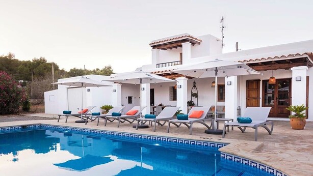 A pool area with lounge chairs and umbrellas, a tiled pool, and a building with a tiled roof and white walls. - Casa Cala LLonga family house 850 m from the beach (Eivissa)