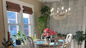 A dining area with a wooden table, white chairs, a chandelier, and potted plants. - 
Welcome to a comfortable, fully furnished 2-bedroom home located mins from  NYC (Bergenfield)