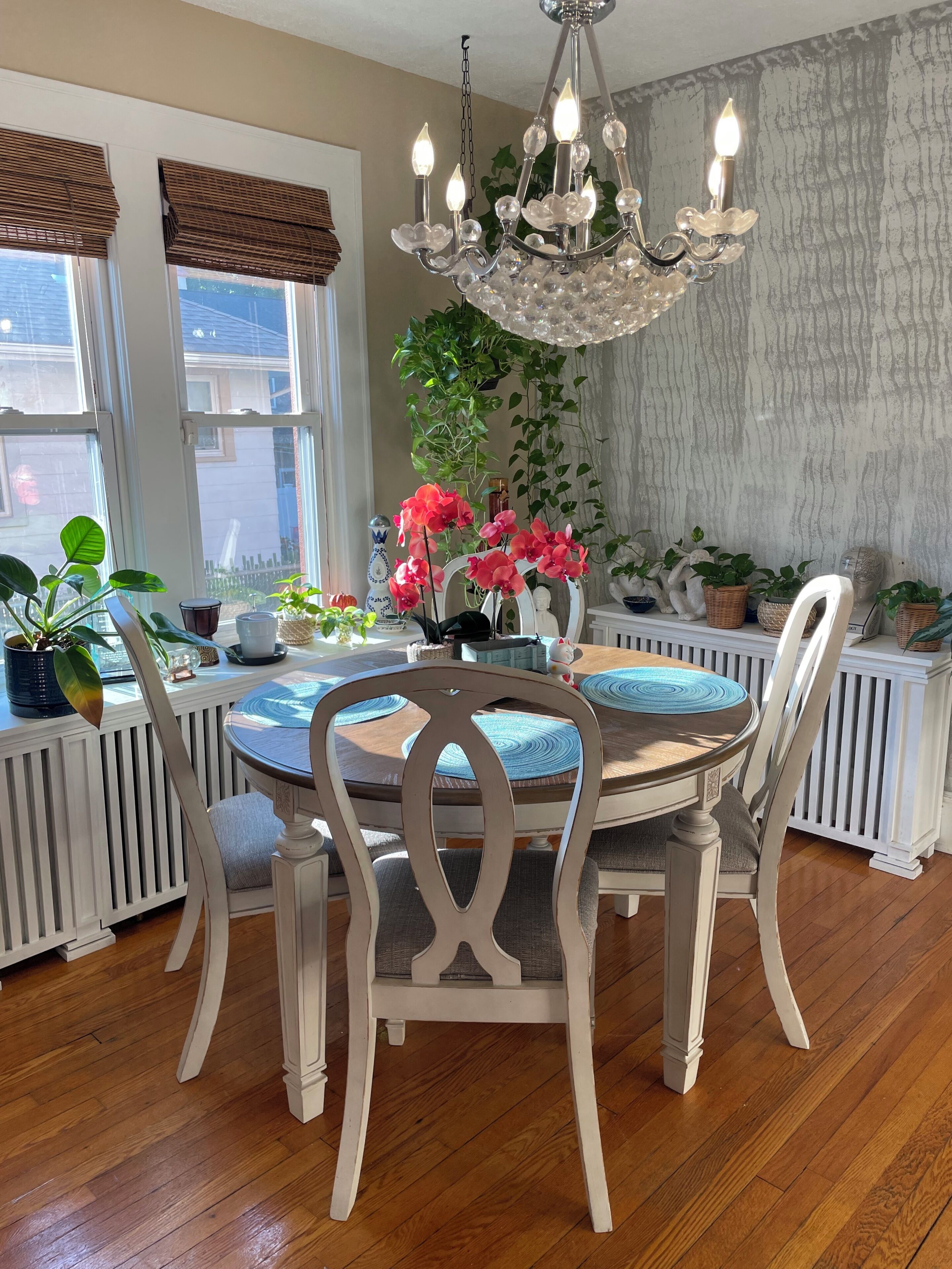 Un comedor con una mesa redonda, sillas blancas, una araña y plantas en macetas.