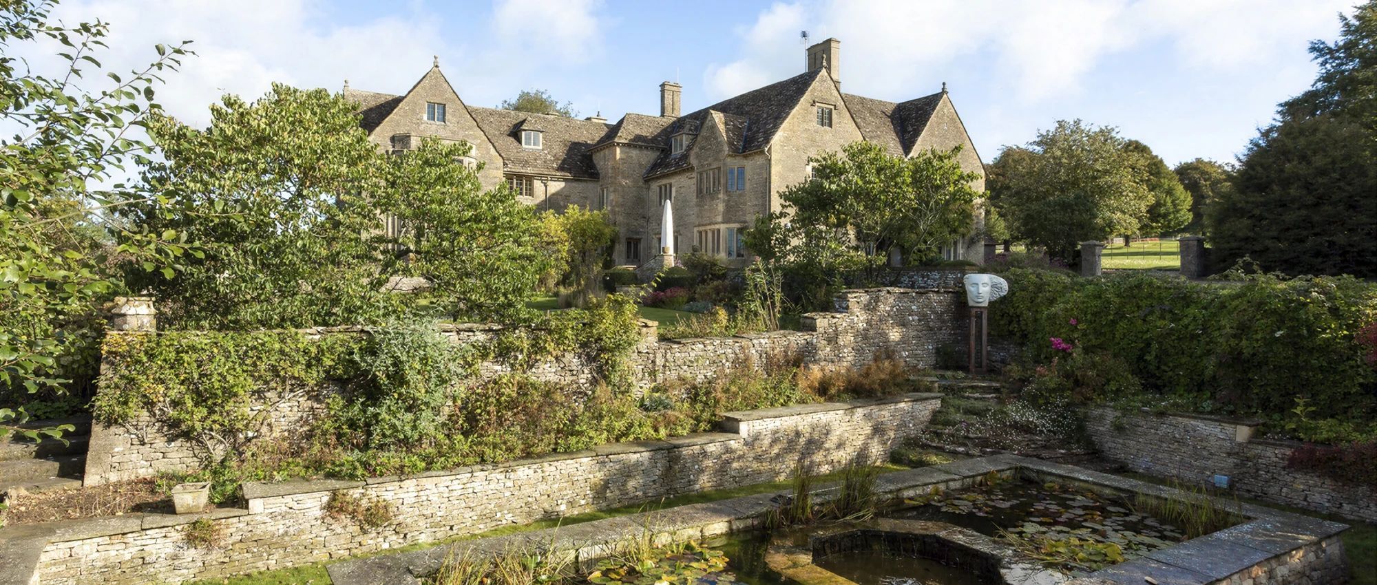Ein historisches Steinhaus mit traditioneller Architektur, umgeben von üppigem Grün und einem kleinen Wasserspiel.