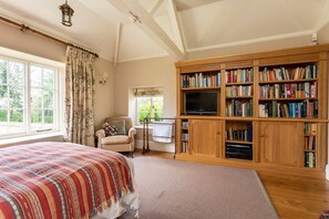 Ein Schlafzimmer mit einem großen Bett, einem Fernseher, einem Bücherregal und einem Fenster mit Vorhängen.