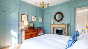 Une chambre à coucher comprenant un lit, une commode, une chaise, une cheminée et un miroir fixé au mur.
