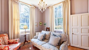 Une pièce avec un canapé à motifs floraux, un fauteuil à motifs, une petite table avec une lampe et un lustre.