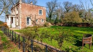 Un bâtiment en briques avec un jardin, un banc et une clôture.