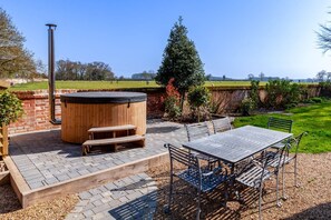 Un patio al aire libre con hidromasaje, bancos de madera, una mesa y sillas.