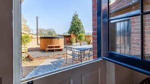 Une vue à travers une fenêtre donnant sur un patio équipé d’un jacuzzi, d’un banc en bois et de meubles pour se détendre en plein air.