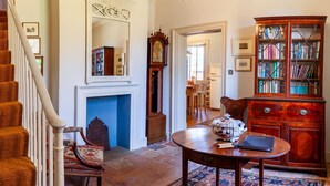 Escada que leva a uma sala de jantar, lareira, armário de madeira com livros e uma mesa com um laptop.