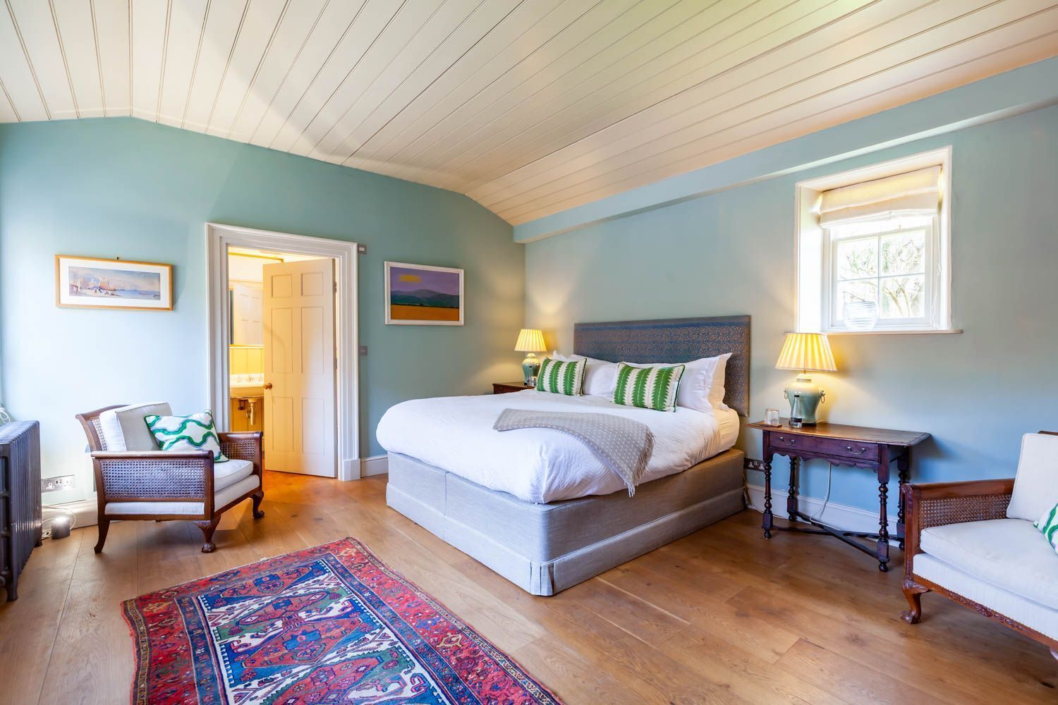 Een slaapkamer met een groot bed, twee nachtkastjes, een stoel, een vloerkleed en een deur.