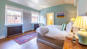 Quarto com cama, abajures, radiador, janela e porta.