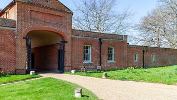 A brick building with a large arched entrance, a gravel path leading to it, and a bench outside.