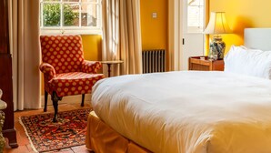 A room with a large bed, a chair, a table, and a window with curtains.