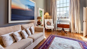 A living room with a sofa, armchair, and a large painting.