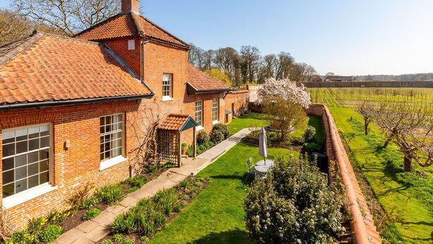 A brick house with a tiled roof, a well-maintained lawn, and a vineyard in the background.