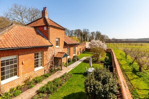 Une maison en briques avec un toit en tuiles, une pelouse bien entretenue et un vignoble en arrière-plan.