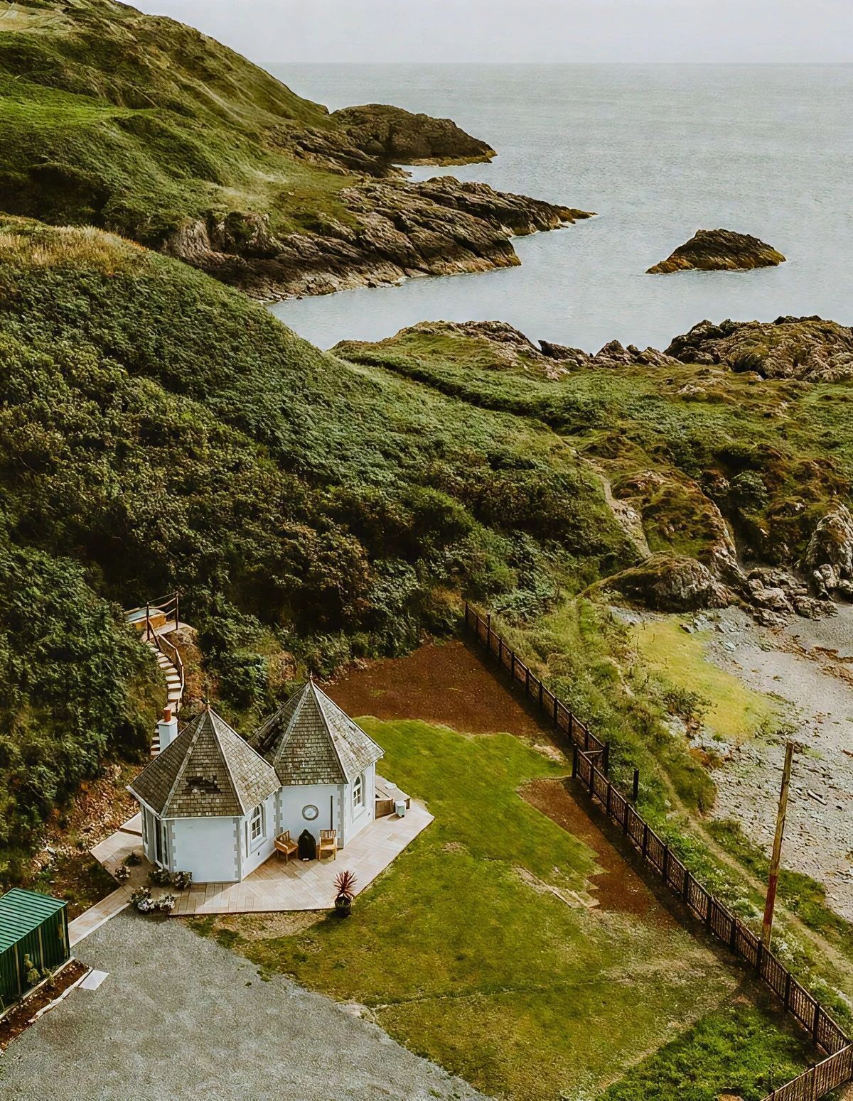 A coastal property with a small white building, a fenced garden, and a view of the sea.