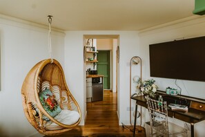 Una habitación con una silla colgante, un escritorio con una computadora y una cocina al fondo.
