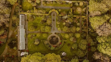 An aerial view of a park with a central circular feature, pathways, and a building with a long, narrow structure on the left.