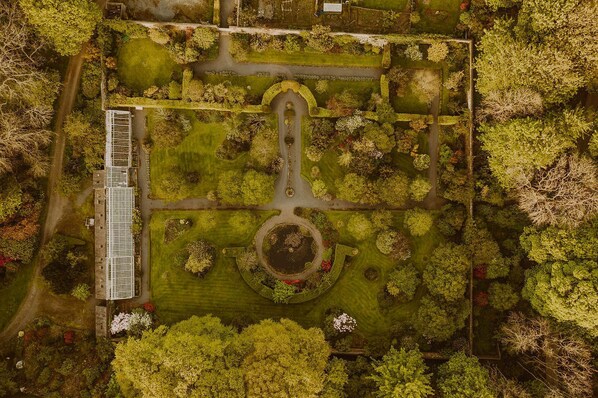 Vista aérea de un parque con un elemento circular central, senderos y un edificio con una estructura larga y estrecha a la izquierda.
