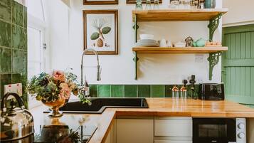 A kitchen with a wooden countertop, a sink, and a dishwasher. There are framed botanical prints on the wall, and a green door is visible in the background.
