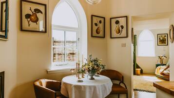 A dining area with a round table, two chairs, a vase with flowers, and framed artwork on the walls.