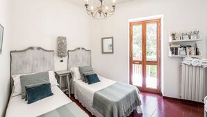 Ein Doppelzimmer mit zwei Betten, einer Kristallleuchtre, einer Holztür und einem Regal mit Handtüchern.