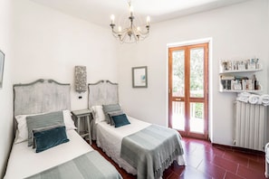 Ein Doppelzimmer mit zwei Betten, einer Kristallleuchtre, einer Holztür und einem Regal mit Handtüchern.