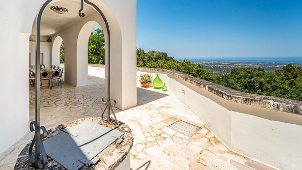 Eine Terrasse mit Steinboden, Grill und Blick auf Stadt und Meer.