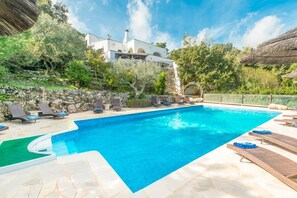 Ein Swimmingpool mit Liegestühlen, eine Steinmauer und ein weißes Gebäude mit einem Strohdach.