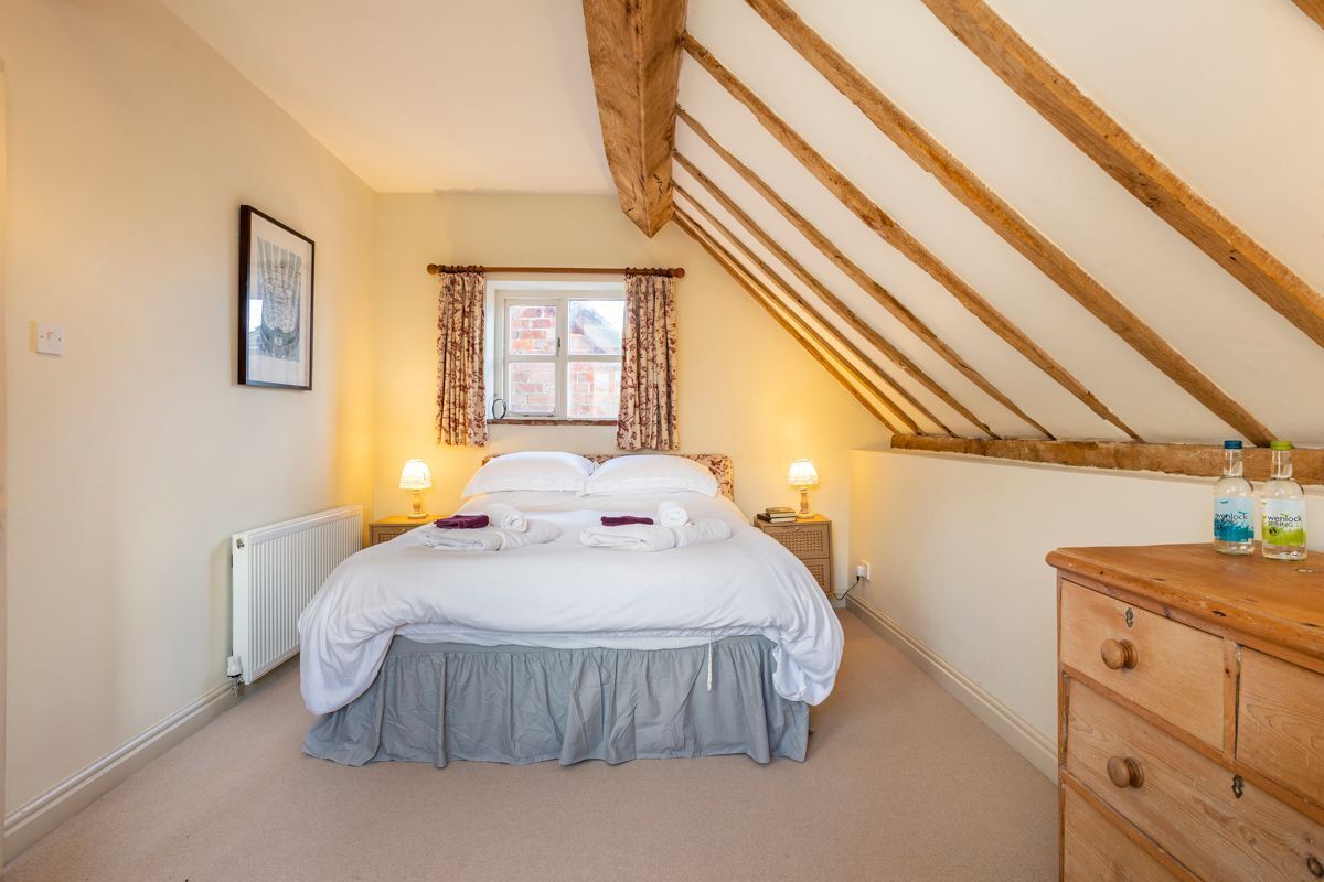 A bedroom with a bed, two bedside lamps, a radiator, a wooden dresser, and a window with curtains.