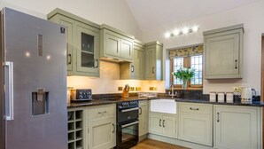 A kitchen with light green cabinets, a stainless steel refrigerator, a black oven, and a window with a plant.