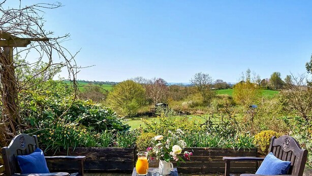 An outdoor seating area with two wooden chairs, a table with a pitcher of orange juice, and a vase with flowers. - Medlar House - Six Bedroom Villa, Sleeps 20 (Cheriton Fitzpaine)