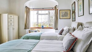 A bedroom with two beds, a window with curtains, a wardrobe, and framed pictures on the wall. - Medlar House - Six Bedroom Villa, Sleeps 20 (Cheriton Fitzpaine)
