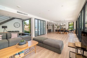 A modern living room with a sofa, ottoman, and coffee table, a dining area with chairs, and a kitchen in the background. - Villa SP1 Suites Santa Ponsa pool wifi (Santa Ponsa)