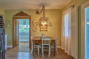 Un'area pranzo con tavolo e sedie in legno, una lampada a sospensione e vista su una cucina attraverso una porta aperta.