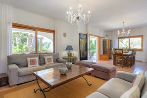 A spacious living area with a sofa, ottoman, wooden coffee table, and dining table with chairs. - Villa Can Colomaret Carmen (Ibiza)