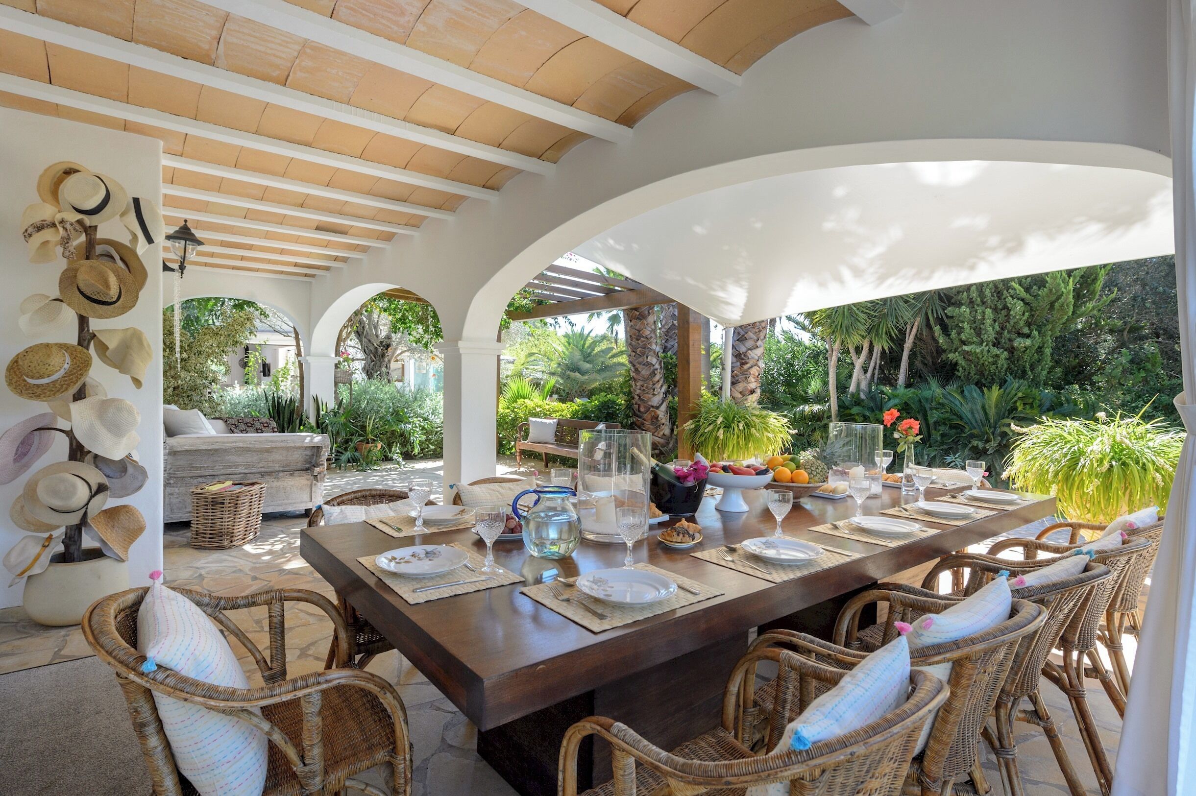 Un área de comedor al aire libre con una mesa larga, sillas de mimbre y diversos utensilios de comedor.