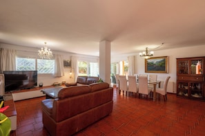 A spacious living room with a leather sofa, a dining area with a table and chairs, a TV, and a chandelier. - New! Villa Lucia - Five Bedroom Villa, Sleeps 8 (Ibiza)