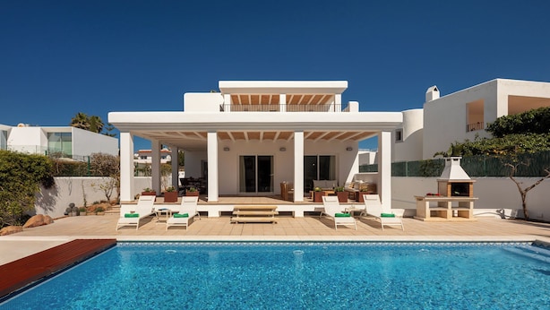 Ein modernes Haus mit Swimmingpool, Sitzgelegenheiten im Freien und einer überdachten Terrasse.