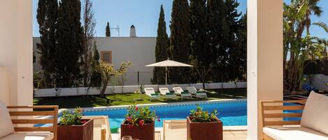 A poolside area with lounge chairs, a table with a bottle and glasses, and planters with flowers.