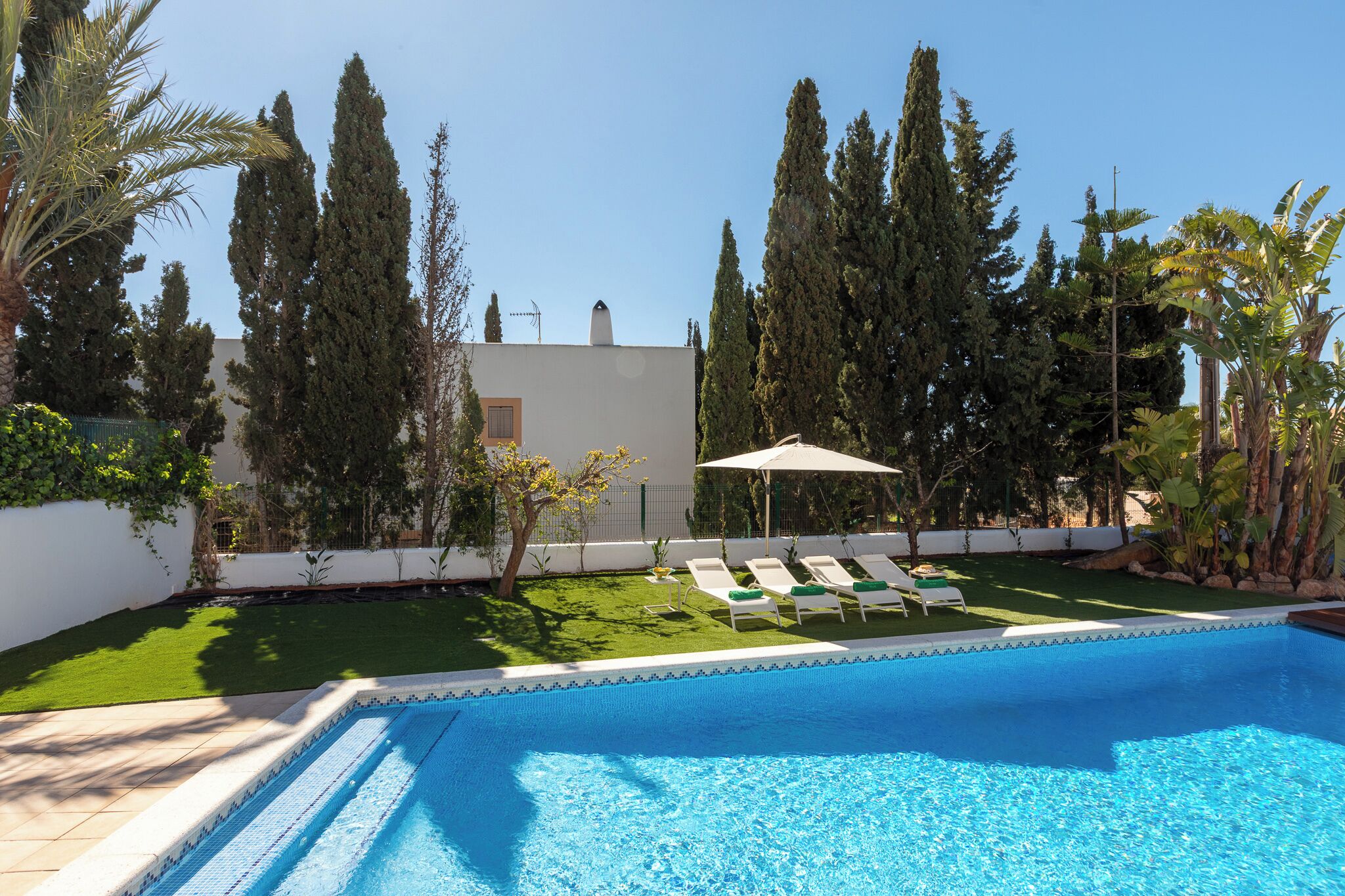 Una piscina con sillones de descanso y un pequeño césped.