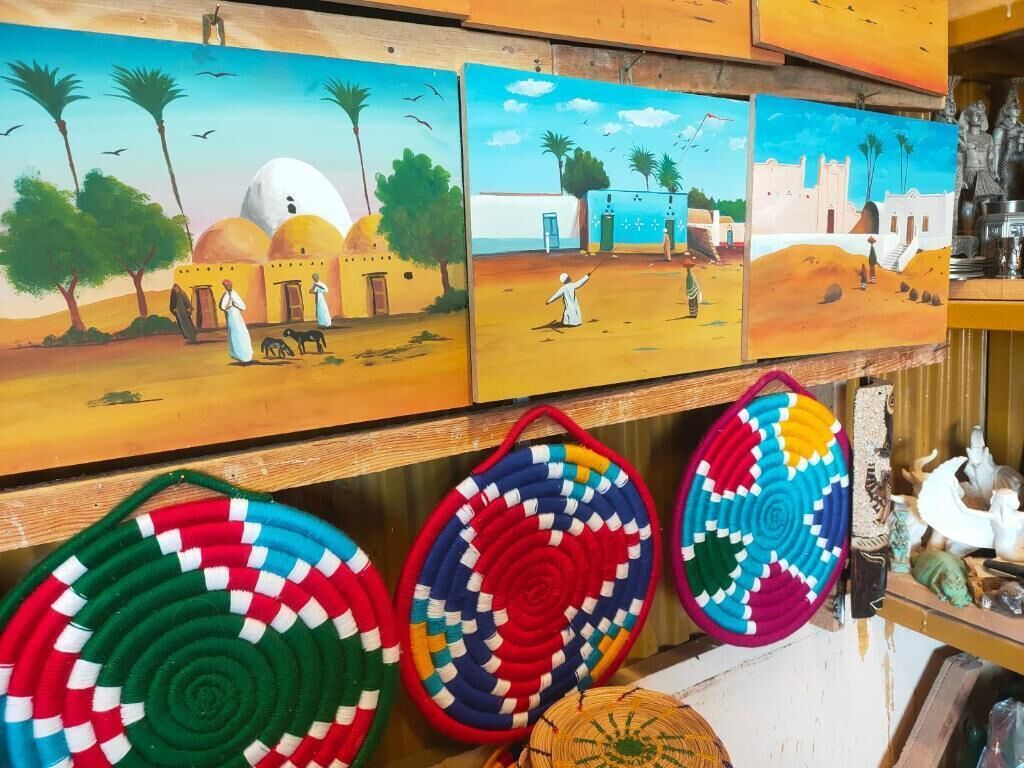 A wall with three paintings depicting desert scenes and three colorful woven mats.