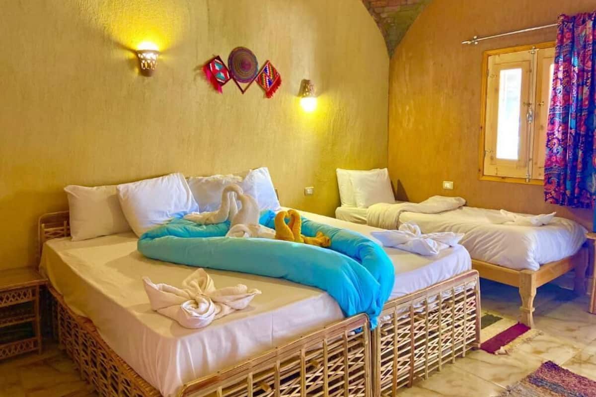 A room with two beds, a brick ceiling, and a window with curtains.
