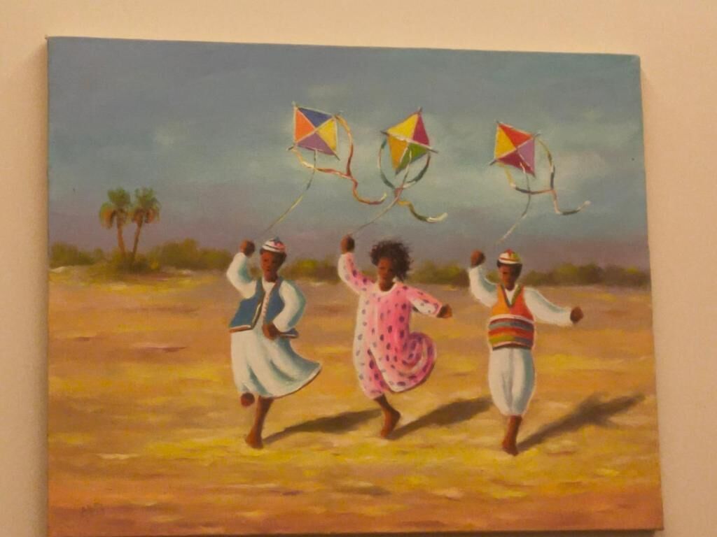Een schilderij van drie mensen in traditionele kleding die vliegeren vasthouden in een woestijnlandschap.