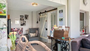 A living room with a sofa, a chair, a table with a sewing machine, and a vase with flowers. - Apartment “Wintergarten Am Thingplatz” with Shared Terrace, Garden & Wi-Fi (Rinteln)