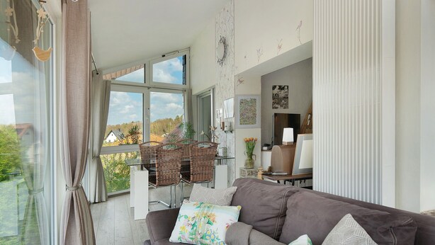 A living room with a brown sofa, a dining area with wicker chairs, and a view of the outdoors. - Apartment “Wintergarten Am Thingplatz” with Shared Terrace, Garden & Wi-Fi (Rinteln)