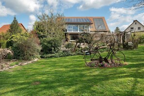 Een huis met een dakbedekt met zonnepanelen, een tuin met een metalen sculptuur, en een houten hek.