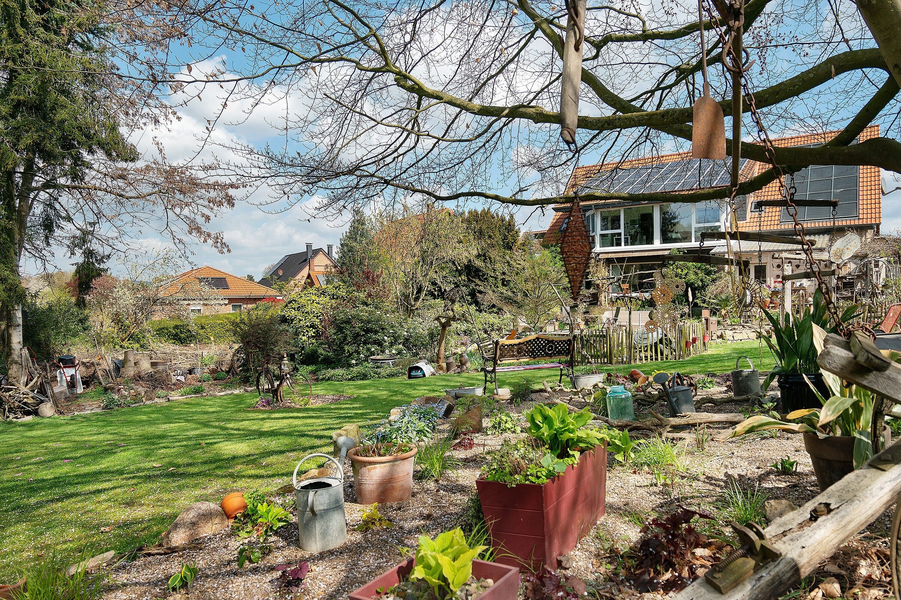 Ein Garten mit verschiedenen Pflanzen und ein Haus mit Solardach.