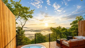 A wooden deck with a hot tub, a wooden sofa, and a view of a mountainous landscape. - Glamping Collective Chattanooga (Trenton)